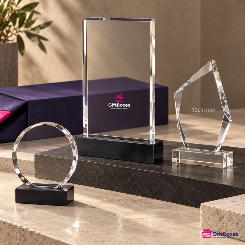 Three crystal awards on black bases — rectangular, circular and faceted peak — in front of a navy presentation box.